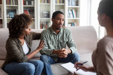 Loving attractive young black woman embracing her depressed frustrated husband looking at copy space, african american couple have therapy session with family psychologist. Marital crisis concept