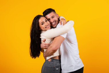 Glad young arabic husband hugging wife at date, enjoy tender moment, look at camera isolated on yellow background, studio. Meeting, family relationship, love and romantic, lifestyle, ad and offer
