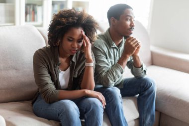 Frustrated millennial african american couple sitting on couch in living room, dont look at each other, looks upset, spouses man and woman feeling down after fight at home, copy space