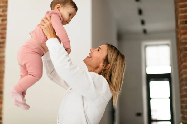 Maternity leave concept. Happy woman spending time with her newborn baby girl, mother playing with child and lifting her up in the air, enjoying motherhood, free space