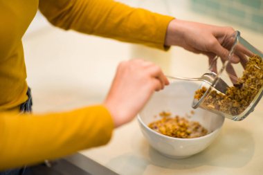 Cropped of female hands making breakfast at home, unrecognizable woman holding bowl with homemade granola at kicthen, closeup shot. Diet, nutrition, detox, healthy lifestyle concept
