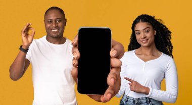 Şuna bak. Mutlu Siyah Adam ve Kadın, Beyaz Ekranlı Akıllı Telefon, Yeni Mobil Uygulama veya Web Sitesi Tanıtımcısı Afro-Amerikan Çifti, Sarı Arkaplanda İzole Edilmiş Poz, Model Model