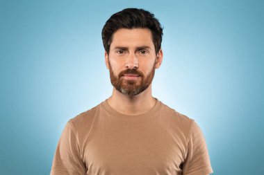 Mavi stüdyo arka planında kameraya poz veren orta yaşlı yakışıklı bir adamın portresi. Tişört giyiyor, boş yer var. Erkek güzellik konsepti