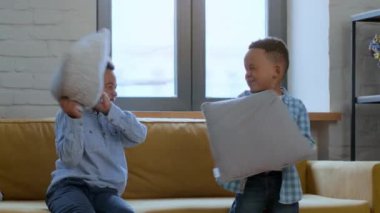 Domestic fun for kids. Cute playful little african american brothers fighting with pillows and laughing, fooling around at home, slow motion, empty space