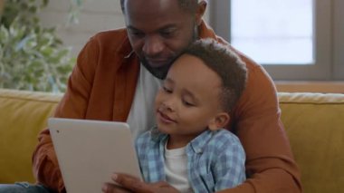 Modern çocuk gelişimi. Sevgi dolu babasıyla dijital tablette eğitim oyunu oynayan küçük, sevimli Afrikalı Amerikalı çocuğun portresi.
