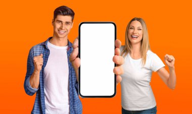 Man And Woman Holding Big Blank Smartphone And Celebrating Success, Cheerful Male And Female Showing Empty Cellphone With Copy Space For Mobile Advertisement, Orange Background, Mockup