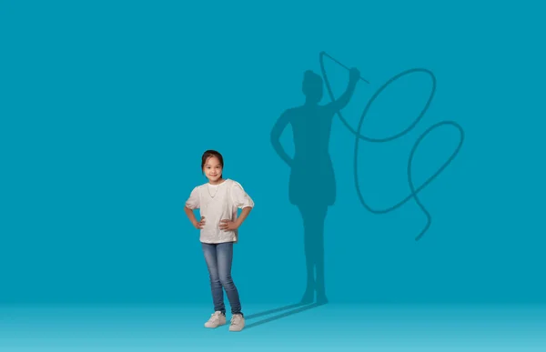 Shadow of female gymnast with tape over cool dreamy pretty asian girl schooler posing on blue studio wall background, copy space, collage. Childhood and big dreams concept
