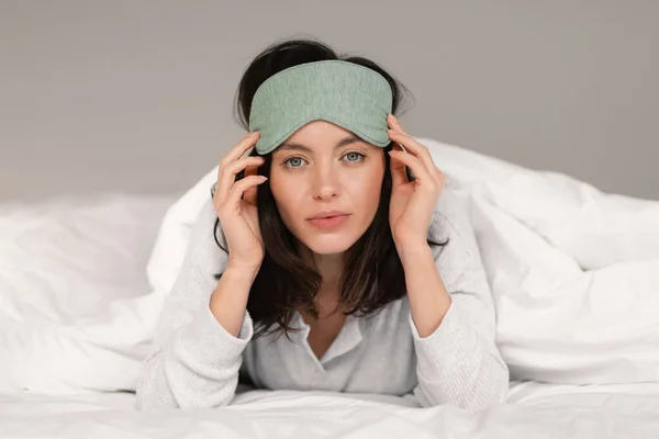 Calm Pretty Caucasian Millennial Female Sleep Mask Lies Bed White — Zdjęcie stockowe