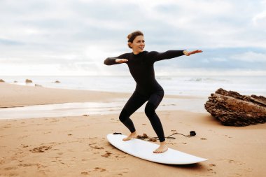 Fit young woman instructor demonstrating how to stand up on surfboard, preparing and practicing on surfboard on beach by seaside, free space