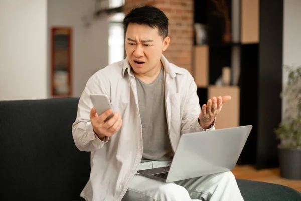 Hombre Coreano Confundido Mirando Pantalla Del Teléfono Celular Sentado Sofá —  Fotos de Stock