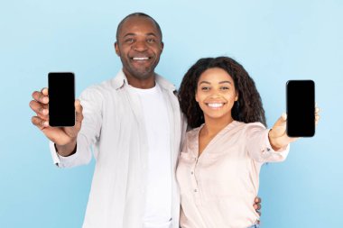 Check this app. Happy black spouses showing two smartphones with empty screens, mock up template, family recommending application or website on mobile phone, blue studio background