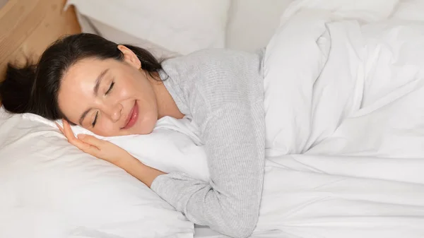 Cheerful caucasian millennial female with closed eyes sleeping on comfortable bed, enjoy softness, weekend, vacation and free time in bedroom interior, panorama, close up. Good morning, rest at home