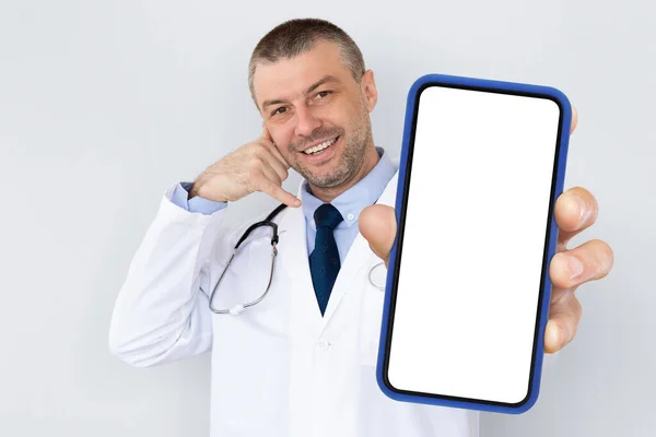 Uśmiechnięty Lekarz Średnim Wieku Pokazujący Pusty Smartfon Wykonujący Gest Profesjonalny — Zdjęcie stockowe