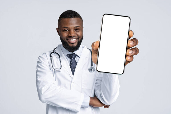 Медицинское предложение. Черный мужчина-врач в униформе демонстрирует смартфон с пустым экраном на камеру, улыбающийся афроамериканец-врач держит пустой сотовый телефон в руке, коллаж, макет