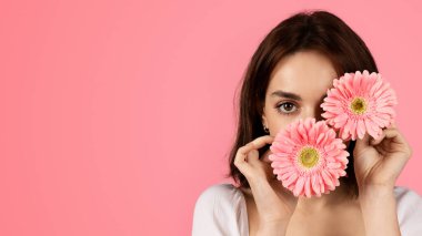 Glad young european woman putting flowers to her face, has fun in free time, enjoy tenderness, isolated on pink background, studio, close up. Holiday, beauty and health care, spa day, ad and offer