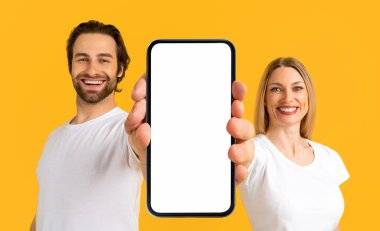Online Offer. Happy Smiling Man And Woman Holding In Hand Huge Blank Smartphone With White Screen, Cheerful Couple Demonstrating Empty Cellphone With Copy Space For Mobile App Design, Mockup