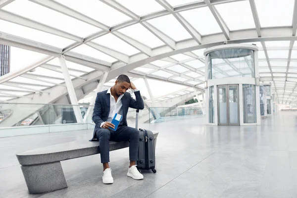 Delayed Flight Concept. Depressed Black Businessman Sitting With Suitcase At Airport Terminal, Portrait Of Upset Young African American Male Entrepreneur Late For Business Meeting, Copy Space