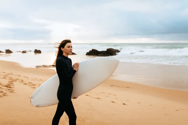 Young beautiful woman with surfboard walking on beach at sunny day, enjoying seaside and active recreation, copy space. Surfer and ocean