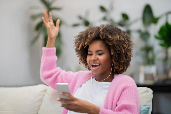 Emotional excited happy millennial black woman with bushy hair and teeth braces sitting on couch at home, checking email on phone, win lottery, female gambling, betting on Internet