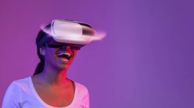 Amazed Black Lady Wearing Glowing VR Headset While Standing In Neon Light Over Purple Studio Background, Excited Happy African American Woman Experiencing Virtual Reality, Panorama With Copy Space