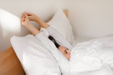 Smiling caucasian millennial lady sleeping on comfortable bed, wake up, stretching body, enjoy softness, weekend, vacation and free time in bedroom interior. Rest and relax at home, good morning