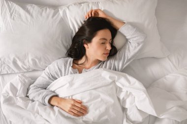 Calm caucasian millennial female sleeps on comfortable bed, enjoy softness, weekend, vacation and free time in bedroom interior, top view, copy space. Rest at home, good morning, relax, sweet dreams