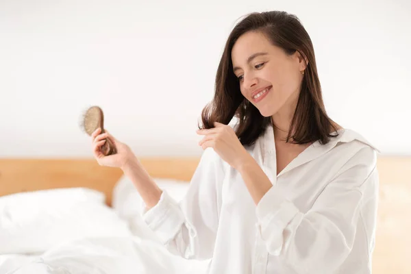 Cheerful Pretty Caucasian Millennial Lady Sits Bed Combs Her Hair — Stok Foto