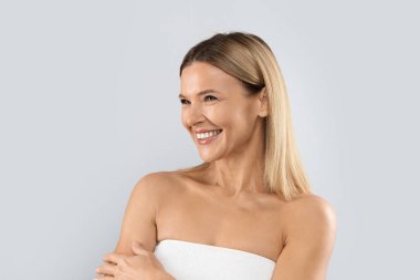 Cheery smiling beautiful middle aged half-naked blonde woman looking at copy space for advertisement, isolated on grey studio background. Aesthetic medicine, cosmetology concept