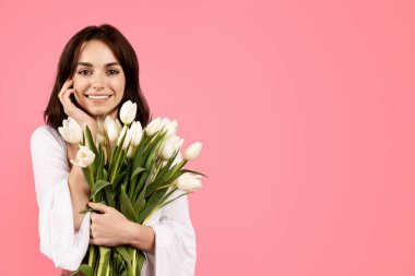 Cheerful young european female with bouquet of tulips, enjoy lifestyle, rejoice spring holiday, celebrate birthday, isolated on pink background, studio. Tenderness, beauty care, gift, ad and offer
