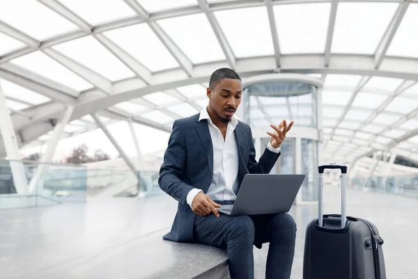 Video Call. Black Businessman Teleconferencing Via Laptop While Sitting At Airport, Young African American Male Entrepreneur In Suit Using Computer For Online Communication, Copy Space
