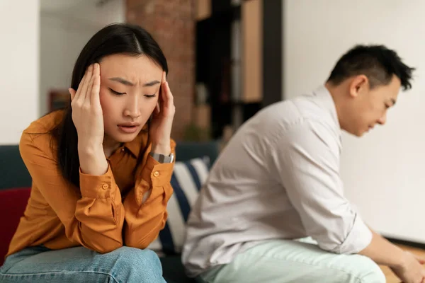 Unhappy young asian woman crying after quarrel with husband, korean couple experiencing difficulties in relationships, sitting on sofa at home