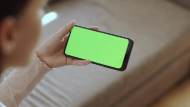Dijital televizyon konsepti. Tanımlanamayan genç bir kadın, yeşil renkli ekranlı akıllı telefondan televizyon izliyor. Modern akış servisinin tadını çıkarıyor. Yavaş çekim, boş alan.