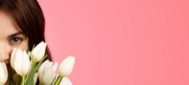 Happy young european female smelling bouquet of flowers, enjoy lifestyle, aroma of tulips, rejoice spring festival, isolated on pink background, studio, panorama. Ad and offer, gift to date, birthday