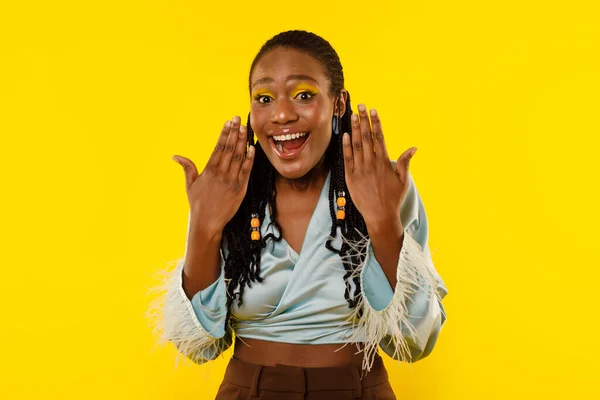 Omg. Excited Black Lady Shouting In Excitement Looking At Camera Posing Holding Hands Near Face On Yellow Studio Background. Female With Bright Makeup Expressing Joy And Positive Emotion. Wow Offer