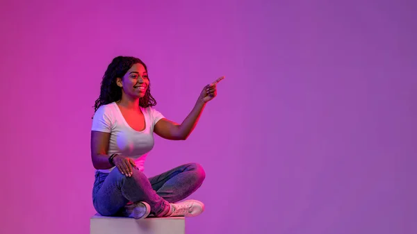 Beautiful Black Woman Sitting Big Cube Neon Light Pointing Aside — Foto de Stock