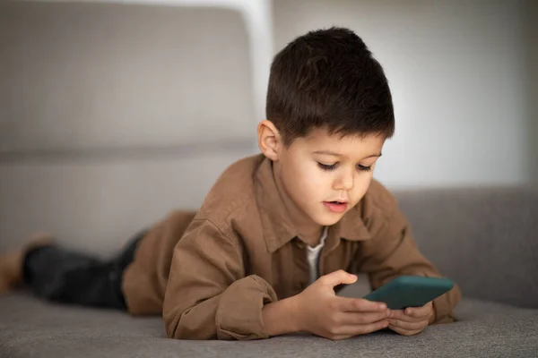 Busy Serious European Small Kid Plays Phone Watches Video Lies — Stockfoto
