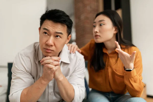 Emotional chinese wife yelling and gesturing at middle aged husband, sitting together on sofa, having difficulties in marriage. Divorce, breakup, crisis in relationship