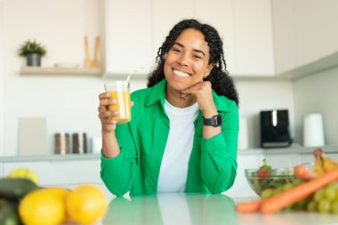 Healthy Nutrition. Cheerful African American Woman Drinking Fresh Orange Juice Holding Glass And Smiling To Camera Sitting At Dining Table In Modern Kitchen At Home. Weight Loss Diet Concept