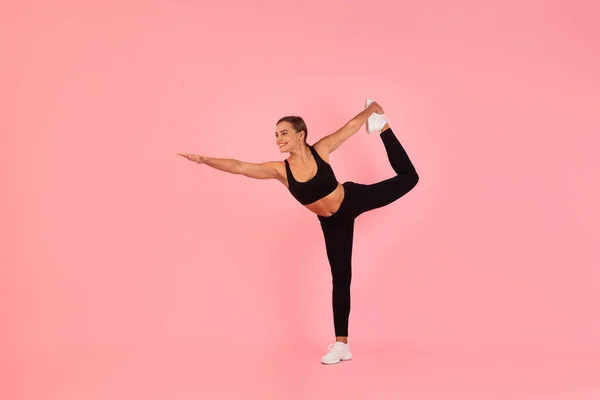 Sporty Young Woman Practicing Balance Exercise, Athletic Female In Sportswear Training Yoga, Stretching Raised Leg And Extending Arm, Standing In Lord Of The Dance Pose Over Pink Background
