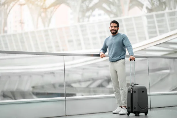 Happy Tourist Man Posing With Travel Suitcase Smiling Looking At Camera Standing At Modern Airport. Transportation And Cheap Tickets Offer Concept. Full Length Shot, Empty Space For Text
