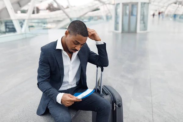 空港でスーツケースを着たアフリカ系アメリカ人ビジネスマンの動揺 飛行機の遅延やキャンセルに苦しむ憂うつな黒人男性起業家 必死に彼の手で旅行チケットを見て — ストック写真