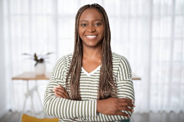 Confident happy attractive young black woman in casual outfit with braided long hair posing at home, holding hands crossed on chest and smiling at camera, copy space. Millennials, successful women