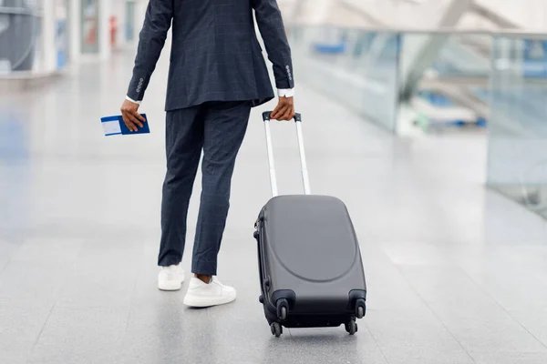 空港でスーツケースを着て歩くスーツ姿の認識できない黒人男性 チケットでパスポートを保持し フライトゲートに行く若いアフリカ系アメリカ人男性旅行者のトリミングされたショット リアビュー — ストック写真