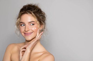 Face skin care. Attractive lady applying cosmetic cream on clean hydrated skin, woman with natural makeup using facial moisturizer, looking aside at free space