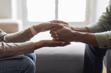 Unrecognizable black woman therapist holding man patient hands against window, giving psychological support while therapy session, cropped indoors shot, closeup, copy space