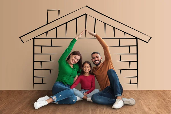 Beautiful mixed race family dreaming about their own house, happy mother and middle eastern father holding hands over their cute little daughter head, sitting on floor over house sketch, collage