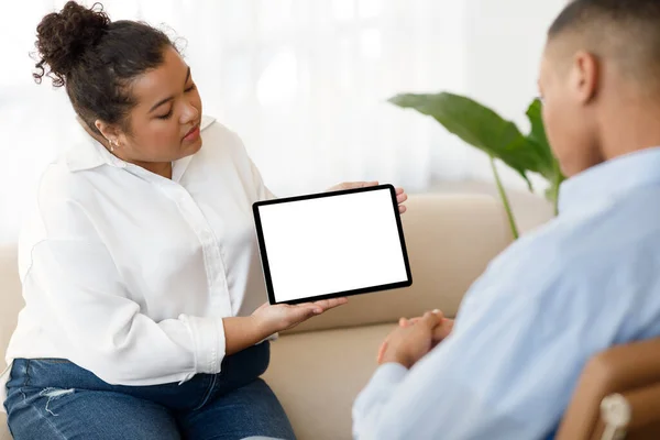 Online therapy app, modern technologies in psychotherapy concept. Mixed race plus size woman therapist showing male patient black guy digital tablet with blank screen during session, mockup