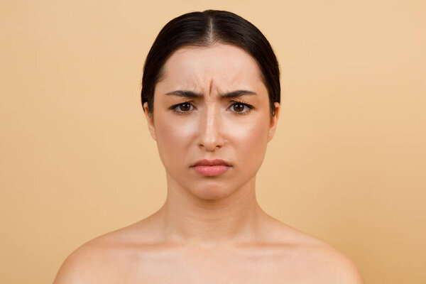 Глабелярные линии. Портрет несчастной молодой индийской женщины, хмурящейся при взгляде на камеру, красивая индуистка с волосами, стоящая в изоляции на фоне бежевой студии, скопировать пространство