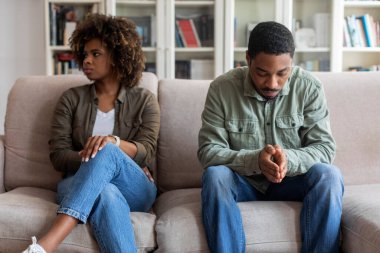 Upset african american millennial man and woman in casual sitting on couch at home, feeling down after quarrel, black spouses having fight, experiencing difficulties in marriage, relationships