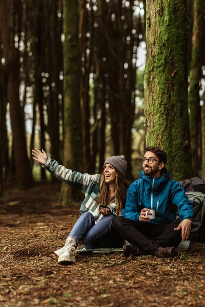 Happy millennial caucasian family in jackets with backpack travel, show hand to cold forest, enjoy adventure together outdoor. Sports at weekend, vacation, active lifestyle and camping, hikers at walk